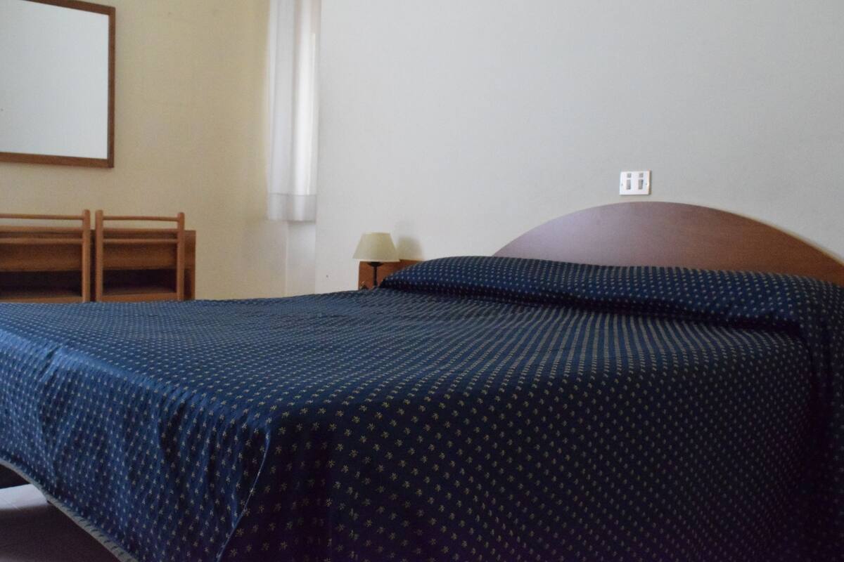 A bedroom with a bed, a nightstand, and a wall-mounted lamp.