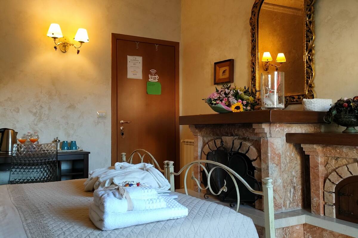 Une chambre d’hôtel équipée d’un lit, d’une cheminée, d’un miroir et de lampes fixées au mur.