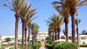 A pathway lined with palm trees leading to a building with multiple balconies and a clear blue sky. - CALIMERA Delfino Beach Resort & Spa - All inclusive (Hammamet)