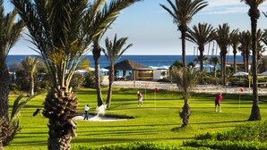 A golf course with palm trees, a water body, and a building in the background. - CALIMERA Delfino Beach Resort & Spa - All inclusive (Hammamet)
