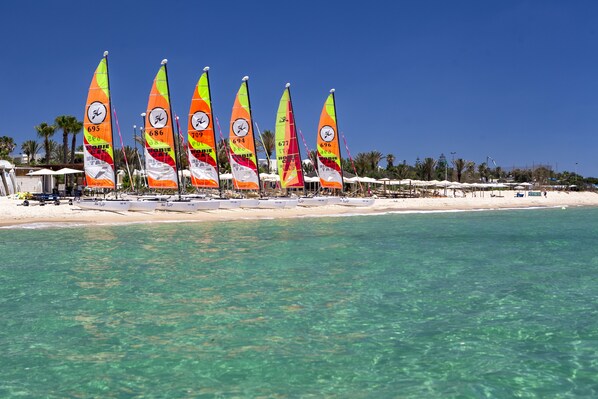 A beach with multiple sailboats lined up on the shore, clear turquoise water, and palm trees in the background. - CALIMERA Delfino Beach Resort & Spa - All inclusive (Hammamet)