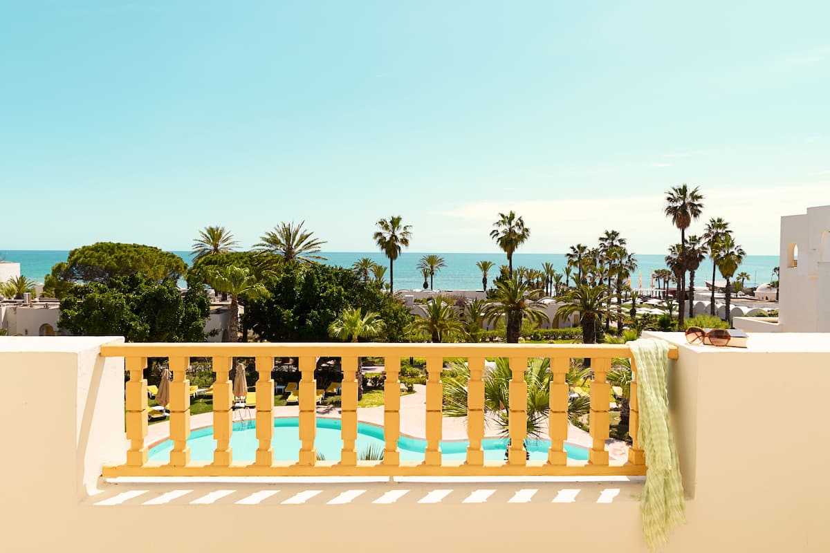 Une piscine bordée d’une rambarde en bois, entourée de palmiers et offrant une vue sur la mer.