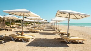 A beach with rows of sun loungers and umbrellas, a clear sky, and the ocean in the background. - CALIMERA Delfino Beach Resort & Spa - All inclusive (Hammamet)