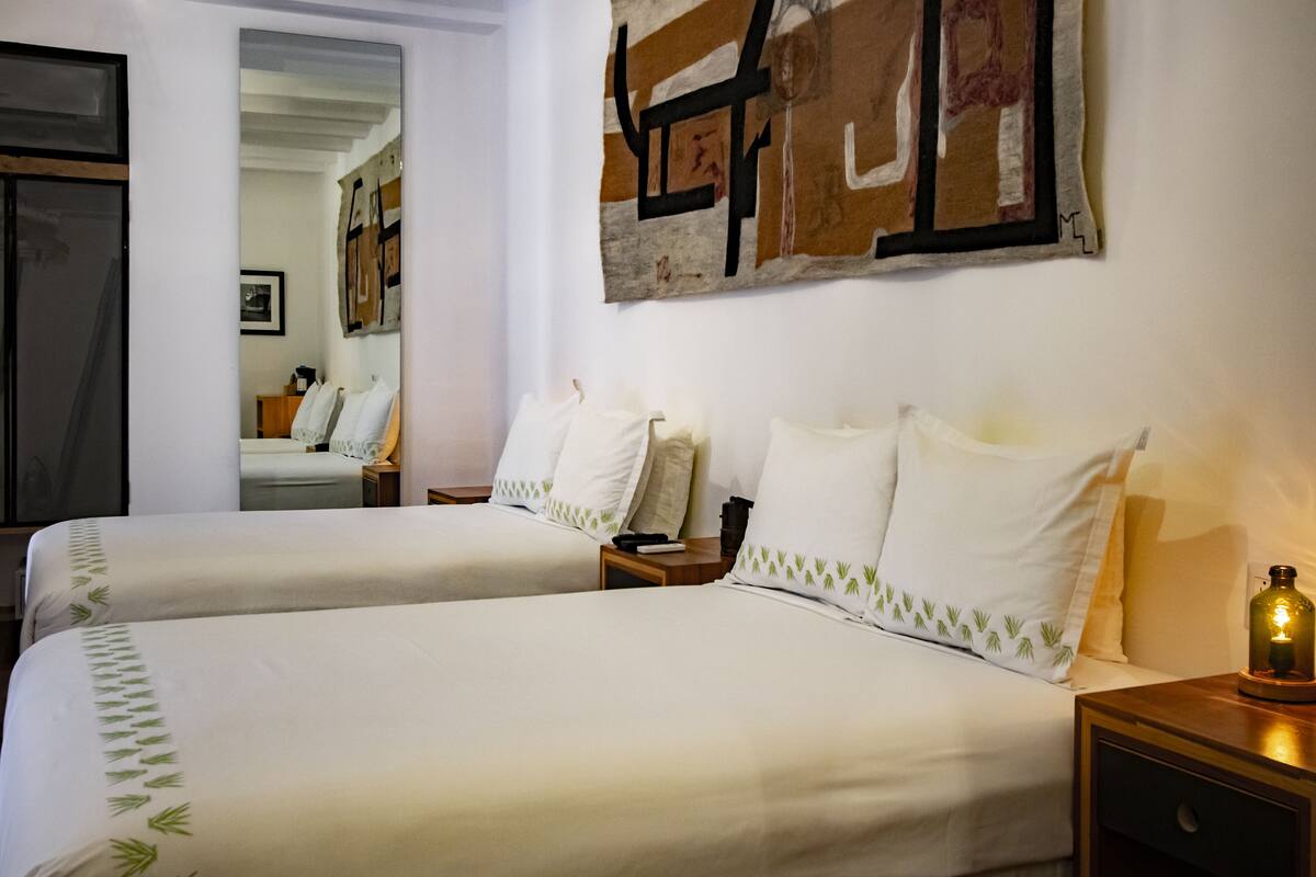 A hotel room with two beds, a large abstract painting on the wall, and a nightstand with a candle.