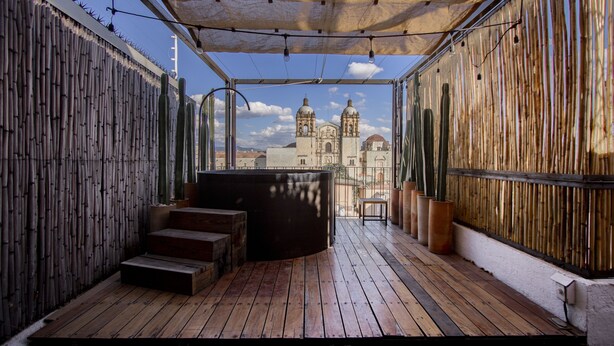 A wooden deck with a sofa and steps, bamboo walls, and a view of a historic building with domes. - Hotel Los Amantes (Oaxaca)