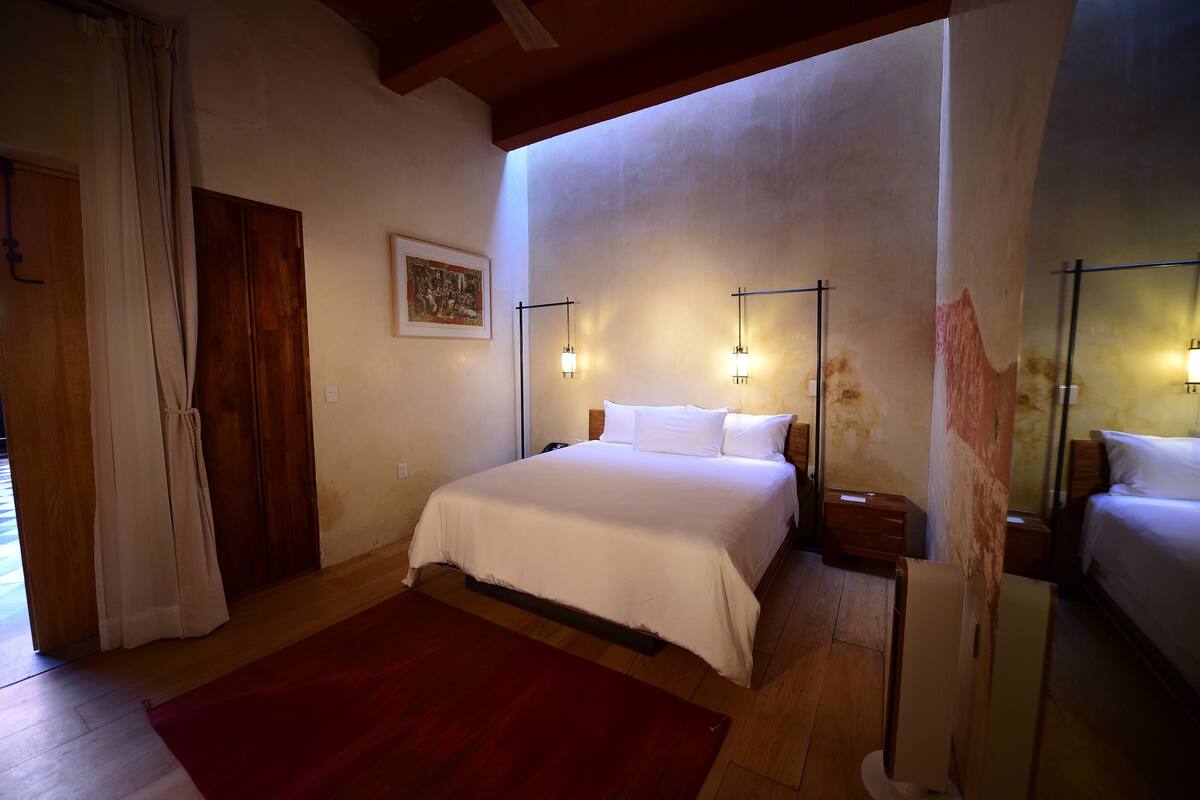 A bedroom with a large bed, wooden floor, a red rug, and two bedside tables with lamps.
