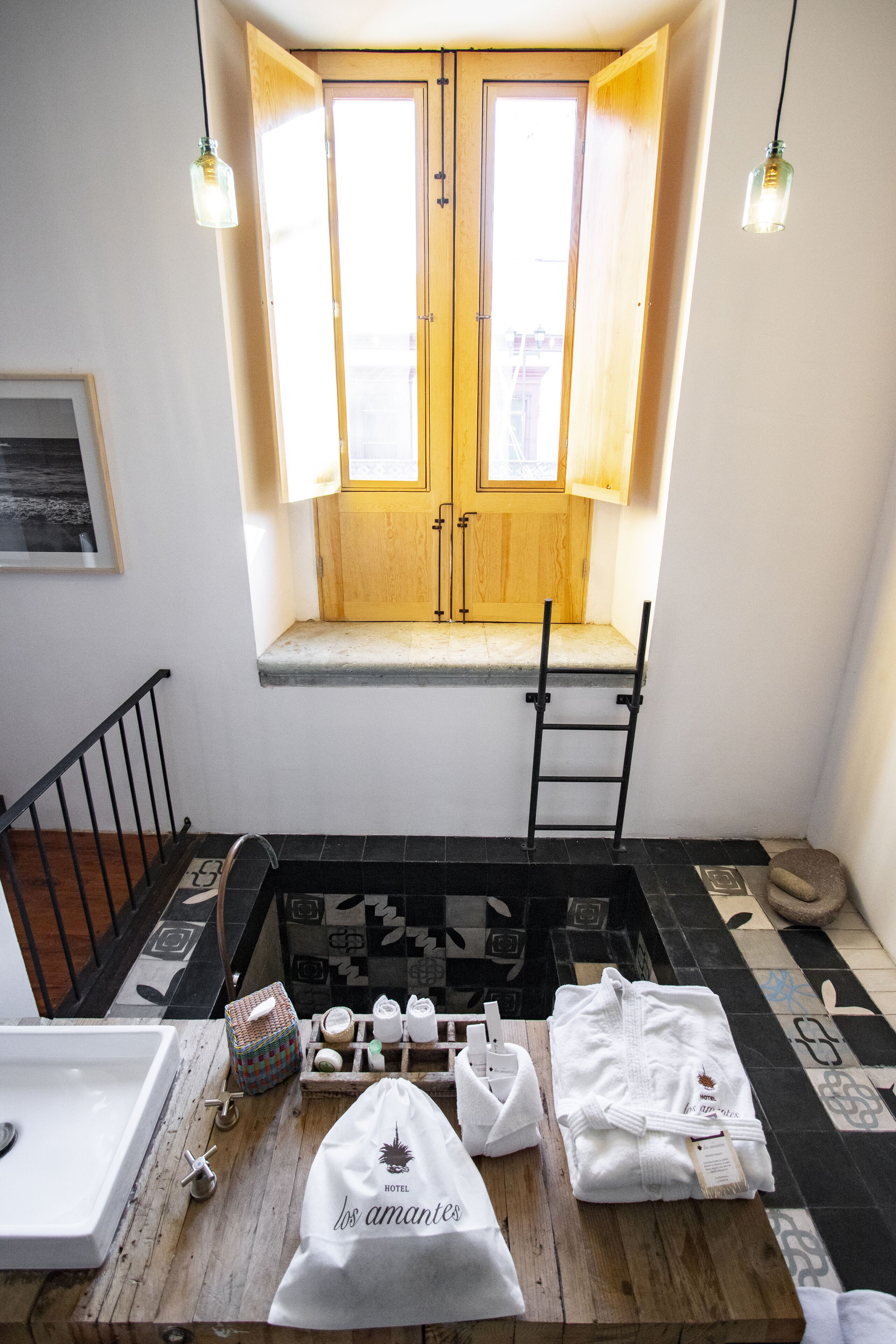 A hotel room with a wooden door, a window with a view, a sink, a towel rack, and a small table with toiletries.