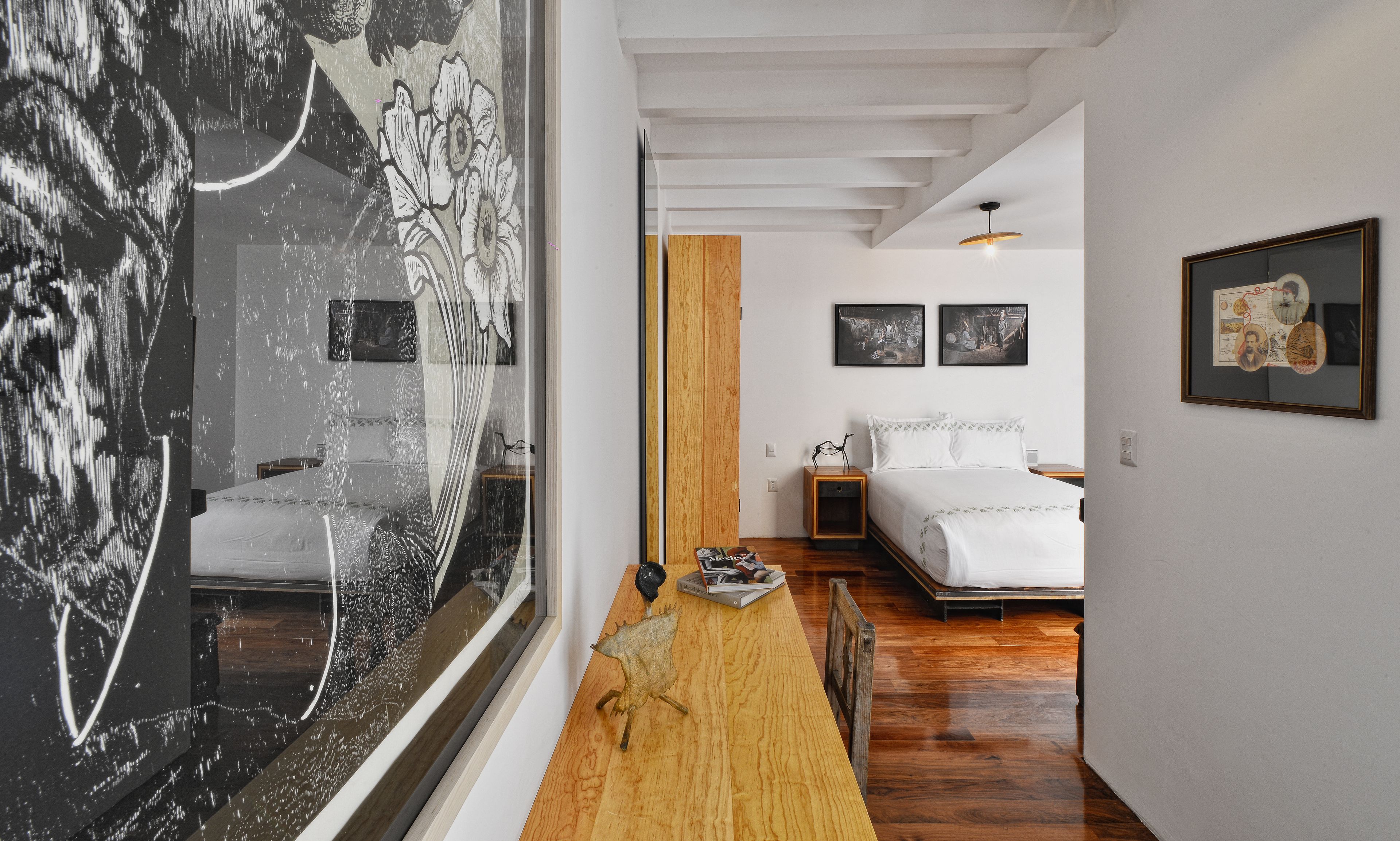 A modern hotel room with a wooden floor, a bed with white bedding, a nightstand, and a wall-mounted artwork.