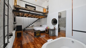 A spacious bedroom with a large bed, a wooden staircase, and a white bathtub. - Hotel Los Amantes (Oaxaca)