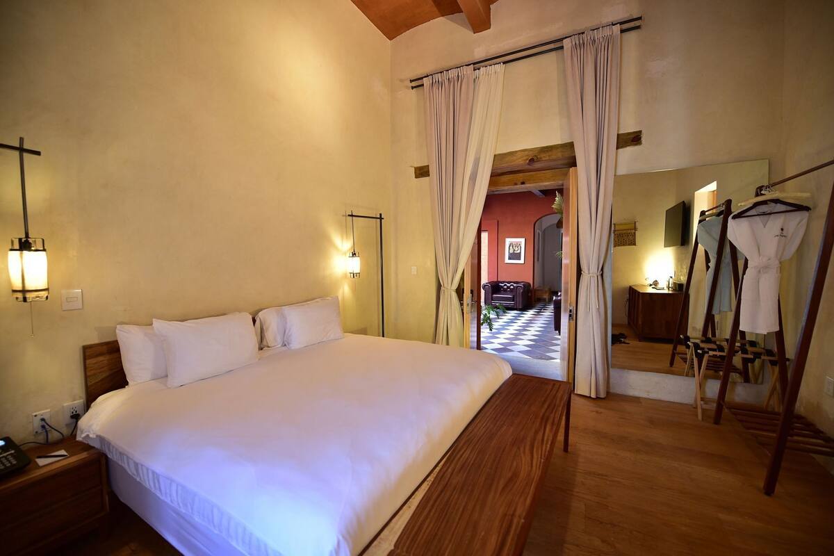 A hotel room with a large bed, bedside lamps, a wooden headboard, a mirror, and a wooden floor.