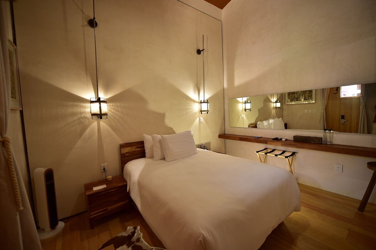 Een hotelkamer met een bed, nachtkastje, spiegel en wandlampen.