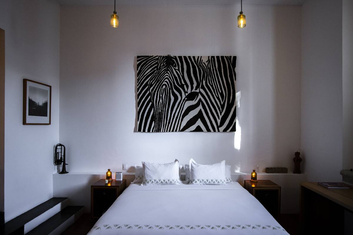 A hotel room with a large bed, two bedside tables, a wall-mounted zebra print, a framed picture, and a small sculpture.