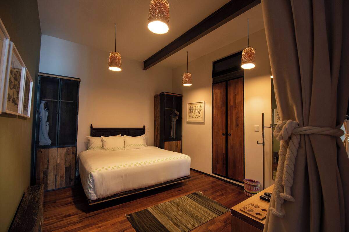 A bedroom with a wooden bed, a nightstand, a wooden wardrobe, and a large window with curtains.