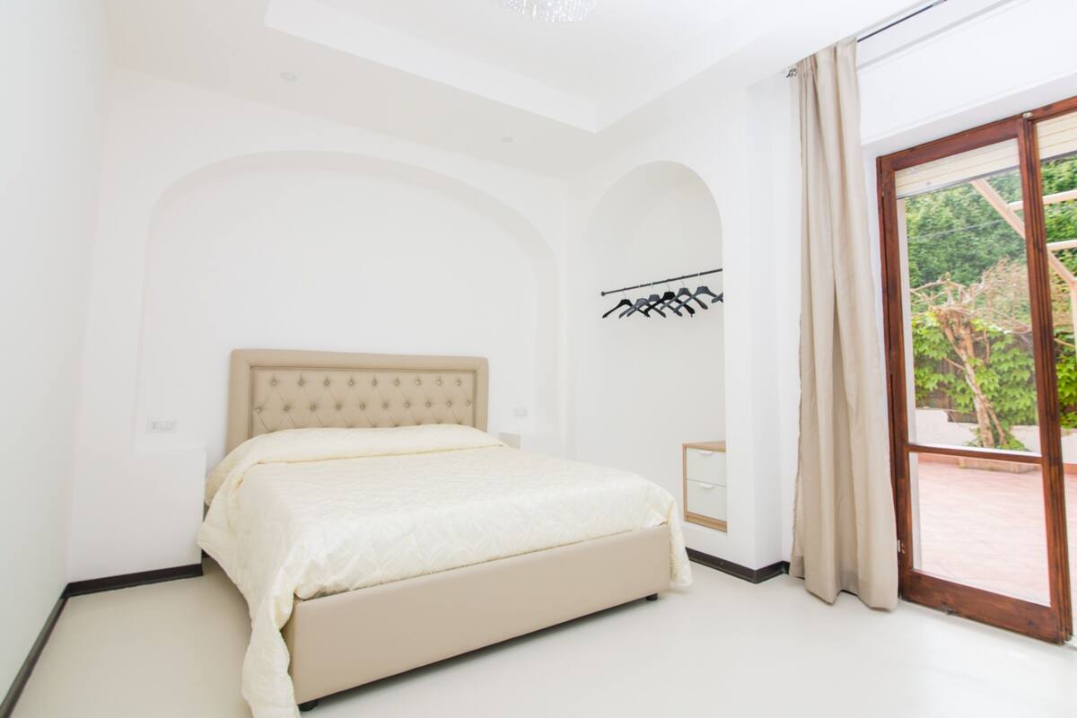 A bedroom with a bed, a wardrobe, and a large window with a view of greenery.