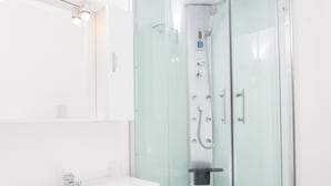 Ein modernes Badezimmer mit einer Glaskabine zur Dusche, einem weißen Waschbecken und einem Schrank.