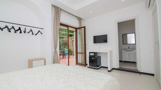 Ein Schlafzimmer mit einem großen Bett, einem an der Wand montierten Fernseher, einem kleinen Kühlschrank und einem Badezimmer mit Waschbecken und Spiegel.