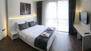 A modern hotel room with a large bed, bedside tables, a desk, and a TV. - Zeytindali Hotel (Trabzon)