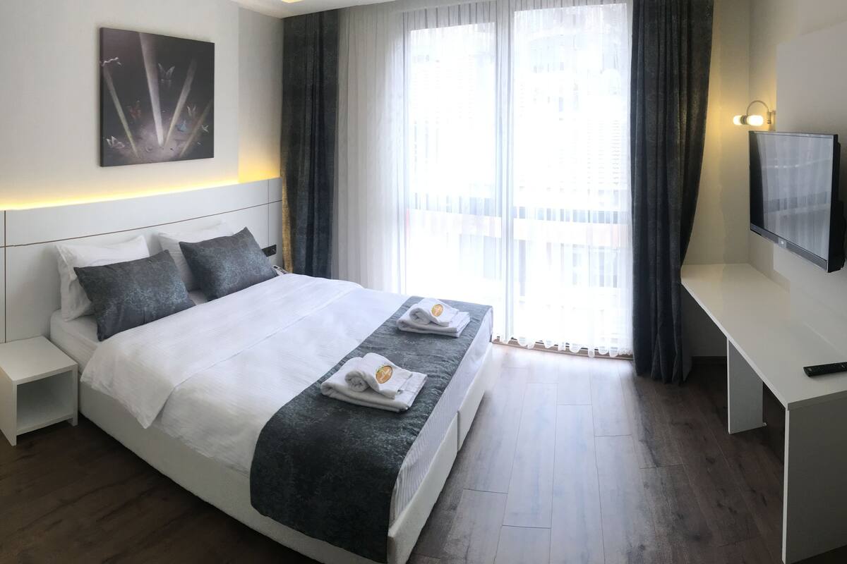 A modern hotel room with a large bed, bedside tables, a desk, and a TV.