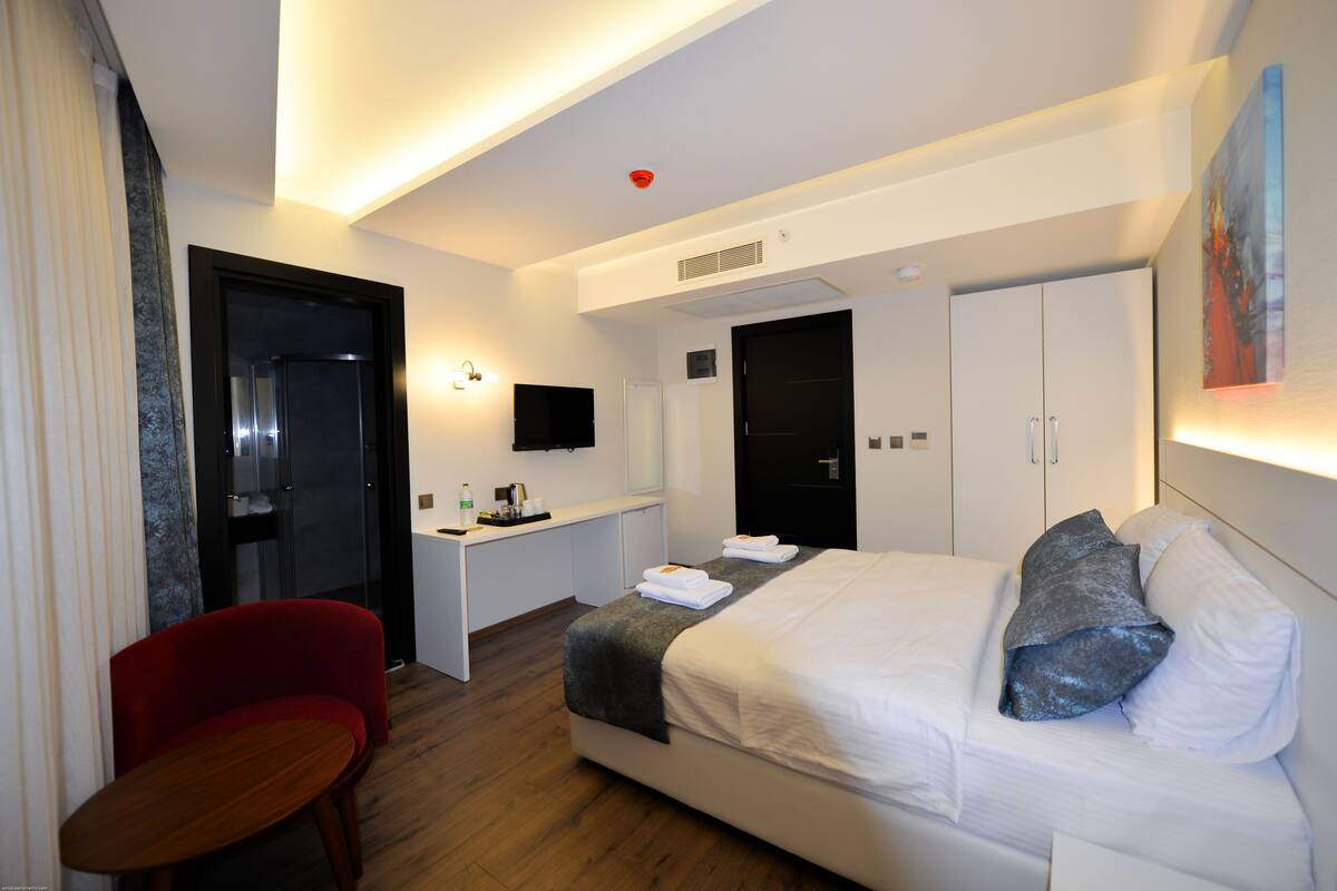 A modern hotel room with a bed, a desk, a chair, and a television.