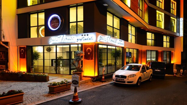 A hotel with a sign reading "guest house" and a logo with three stars. There are two cars parked in front, and a potted plant is visible on the sidewalk. - Zeytindali Hotel (Trabzon)