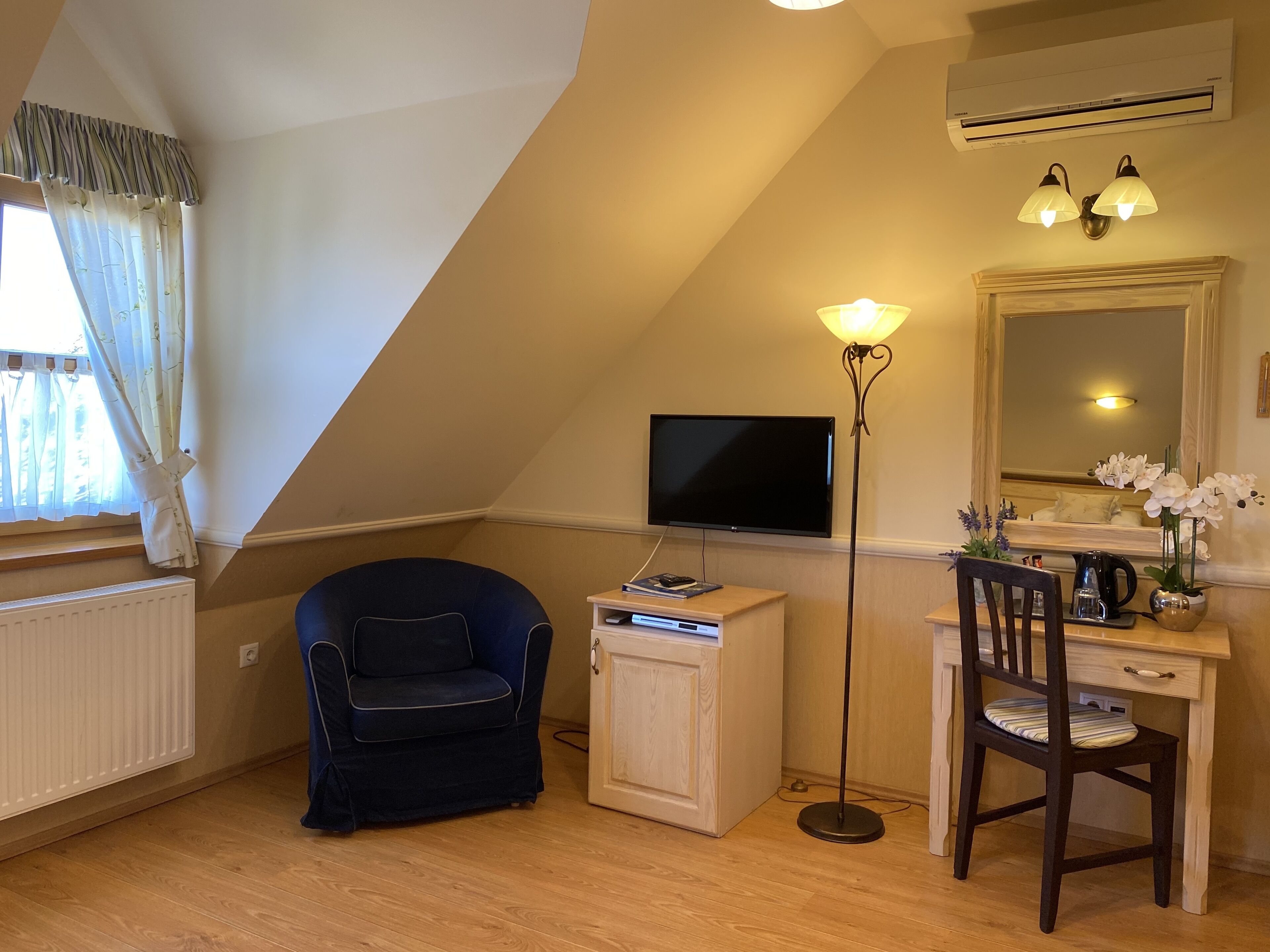 A cozy room with a TV, a desk, a chair, and a floor lamp.