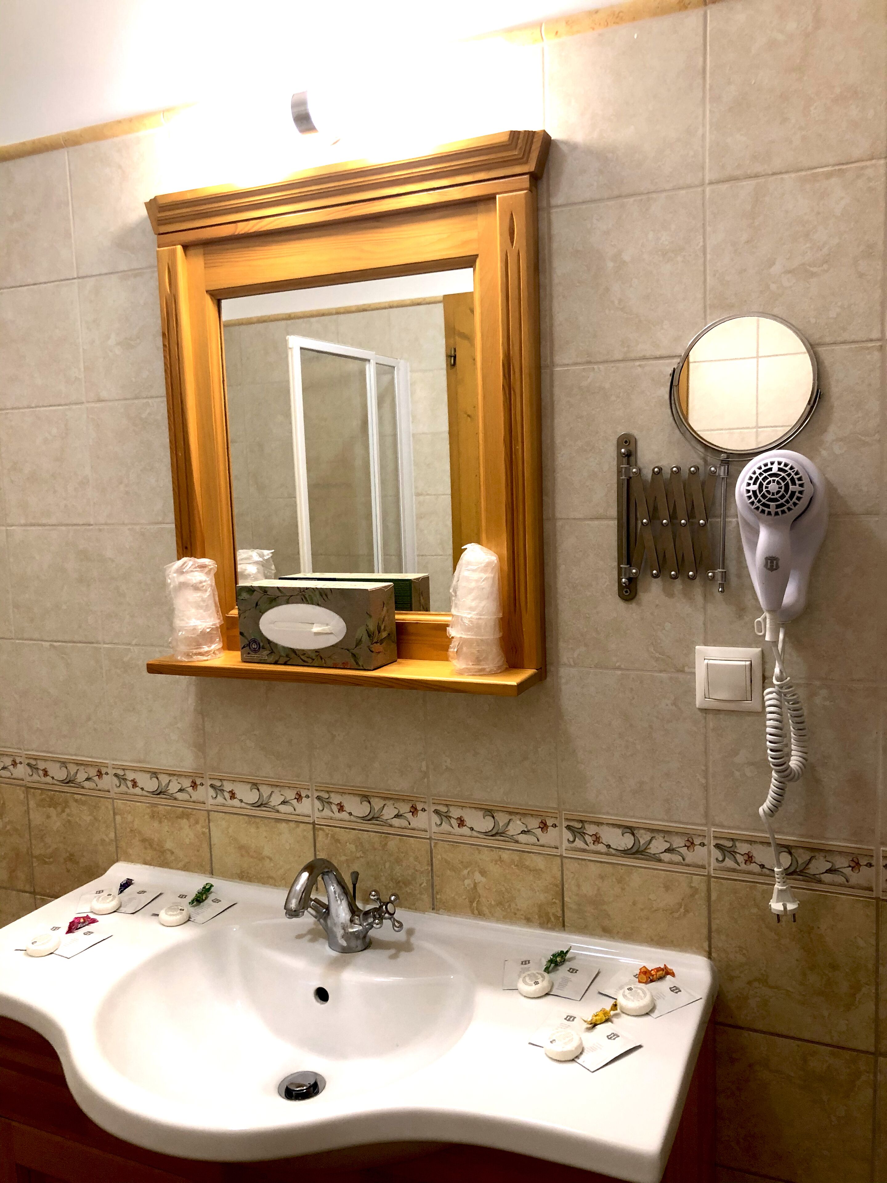 Un baño con un lavamanos blanco, un espejo, un secador de pelo y artículos de tocador en la pared.
