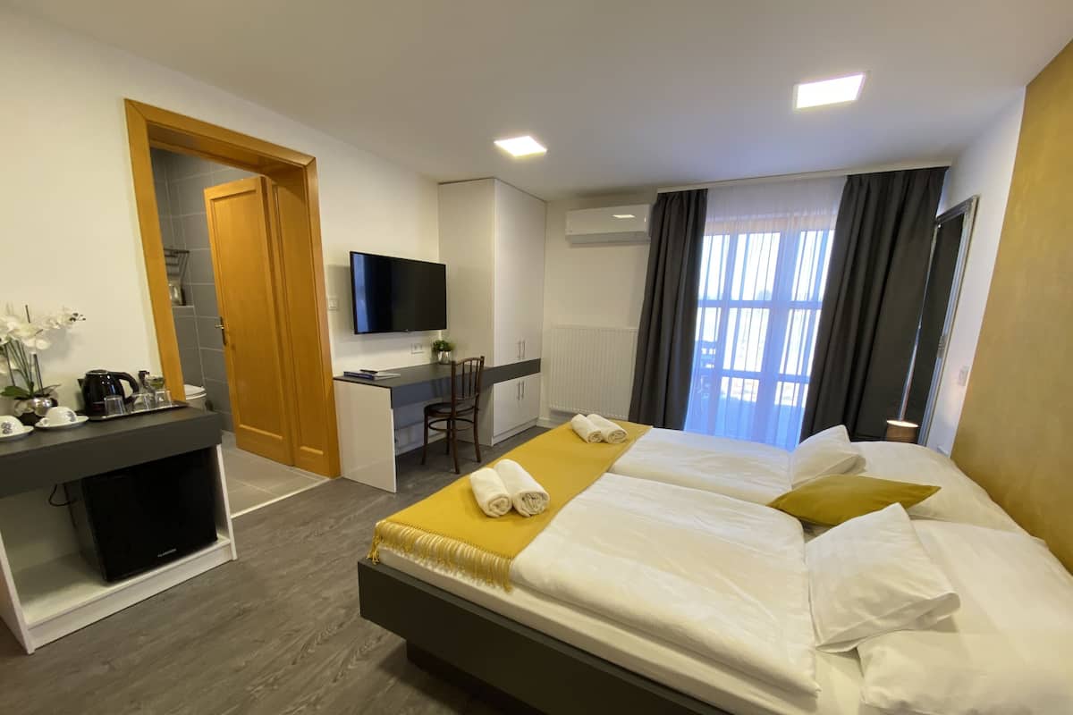 Habitación de hotel con cama, escritorio, televisor y ventana con cortinas.