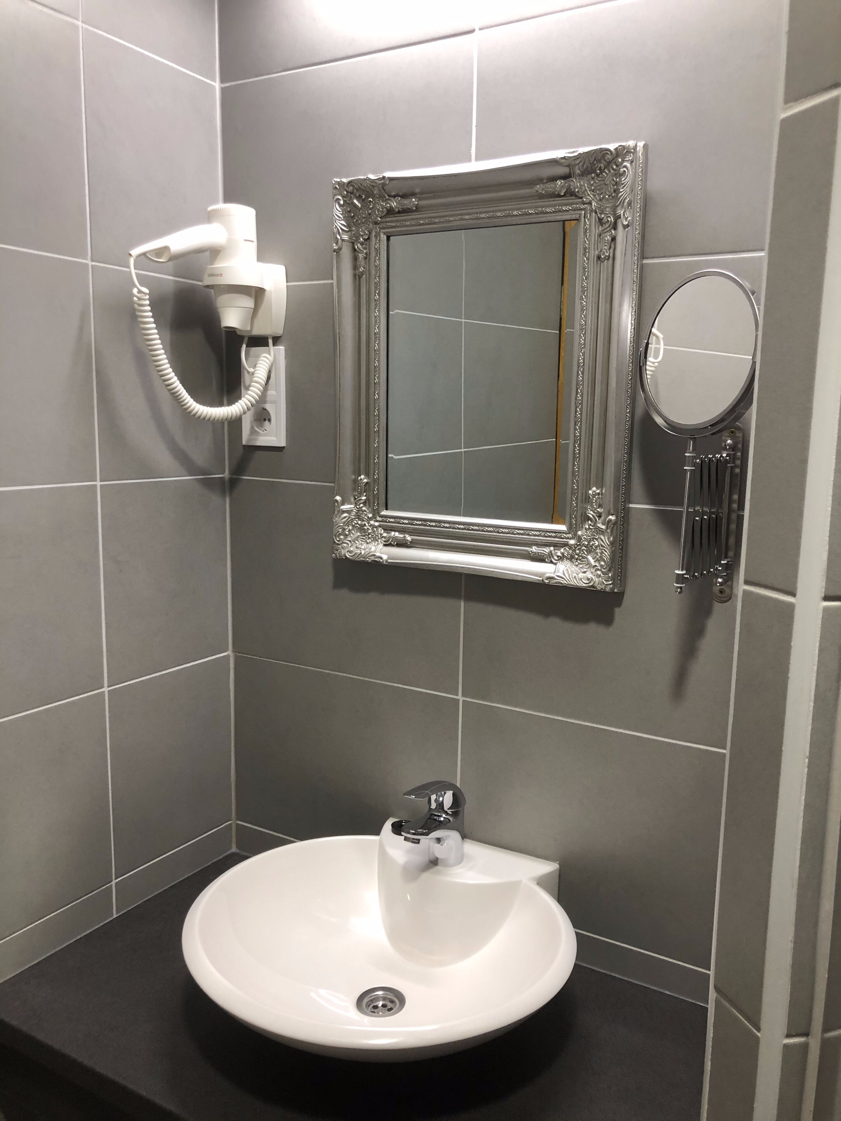A bathroom with a white sink, a mirror, and a hairdryer on the wall.
