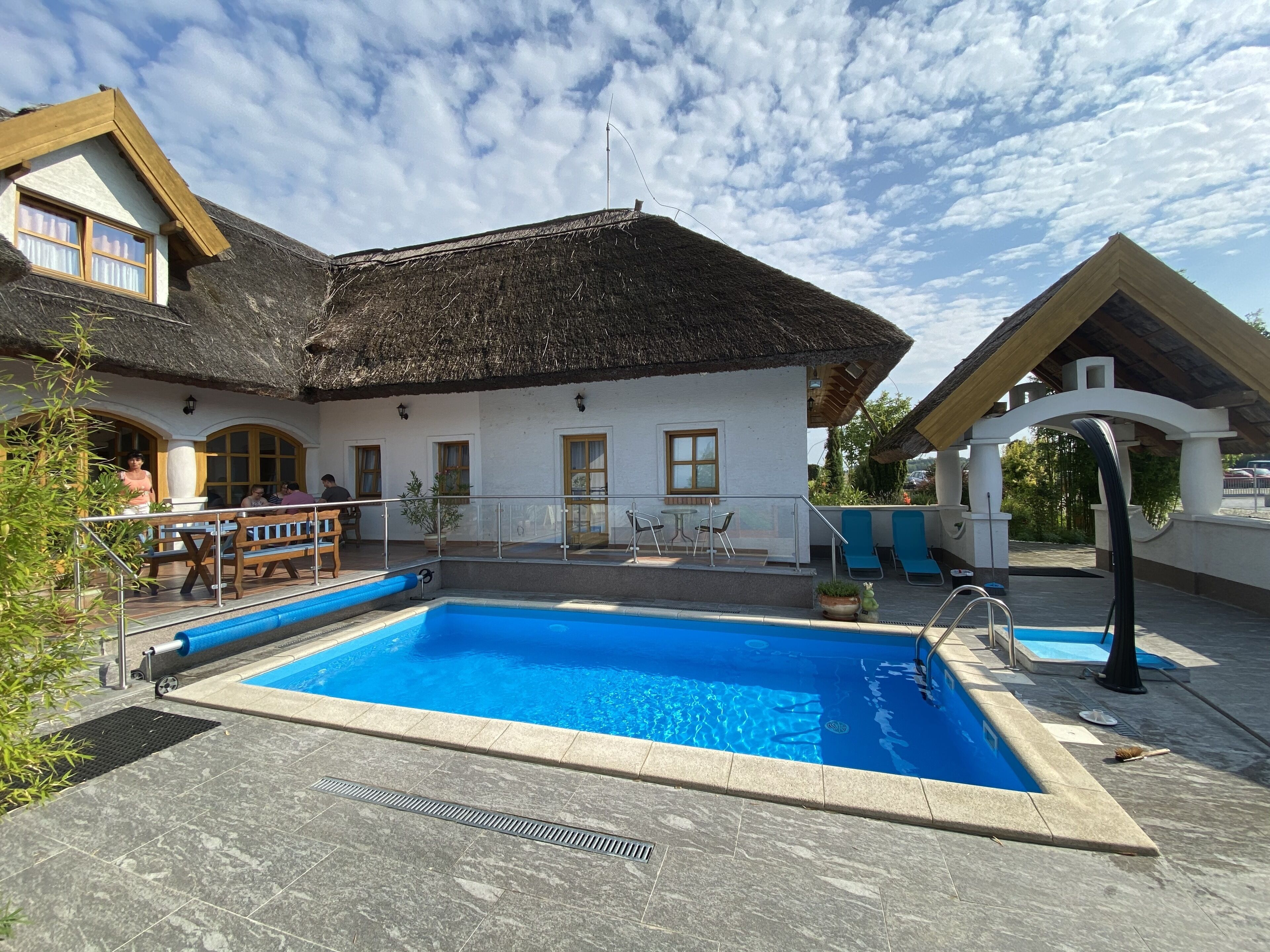 A pool area with a thatched-roof building, outdoor seating, and a clear sky.