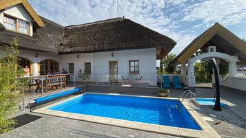 A pool area with a thatched-roof building, outdoor seating, and a clear sky.