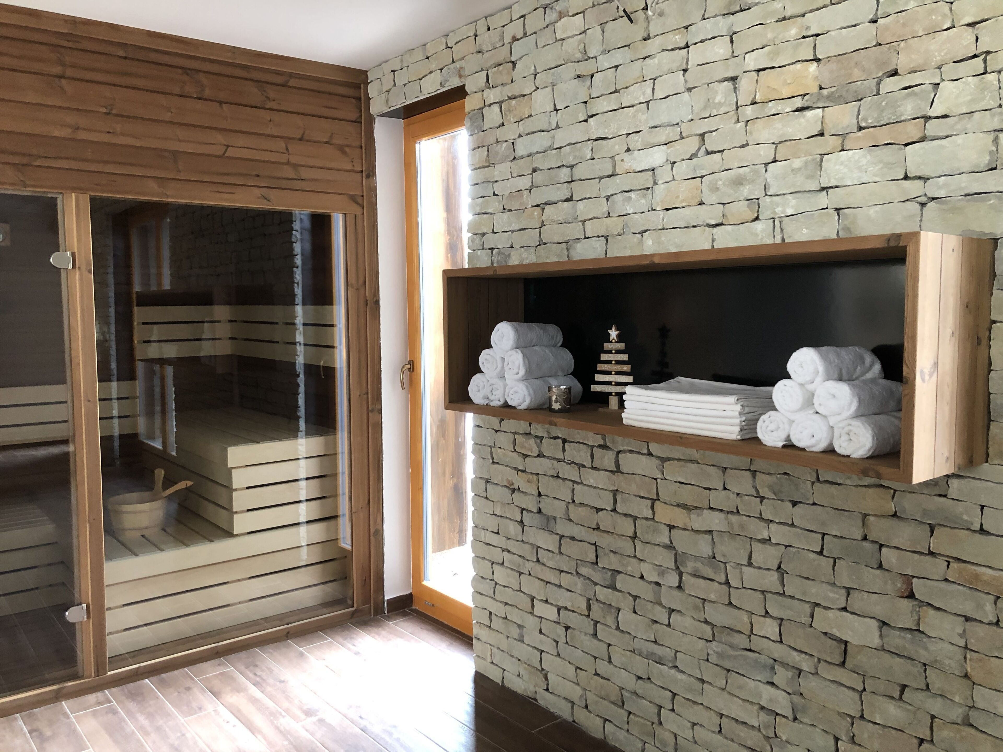 A room with a stone wall, wooden shelves with towels, and a sliding glass door leading to a balcony.