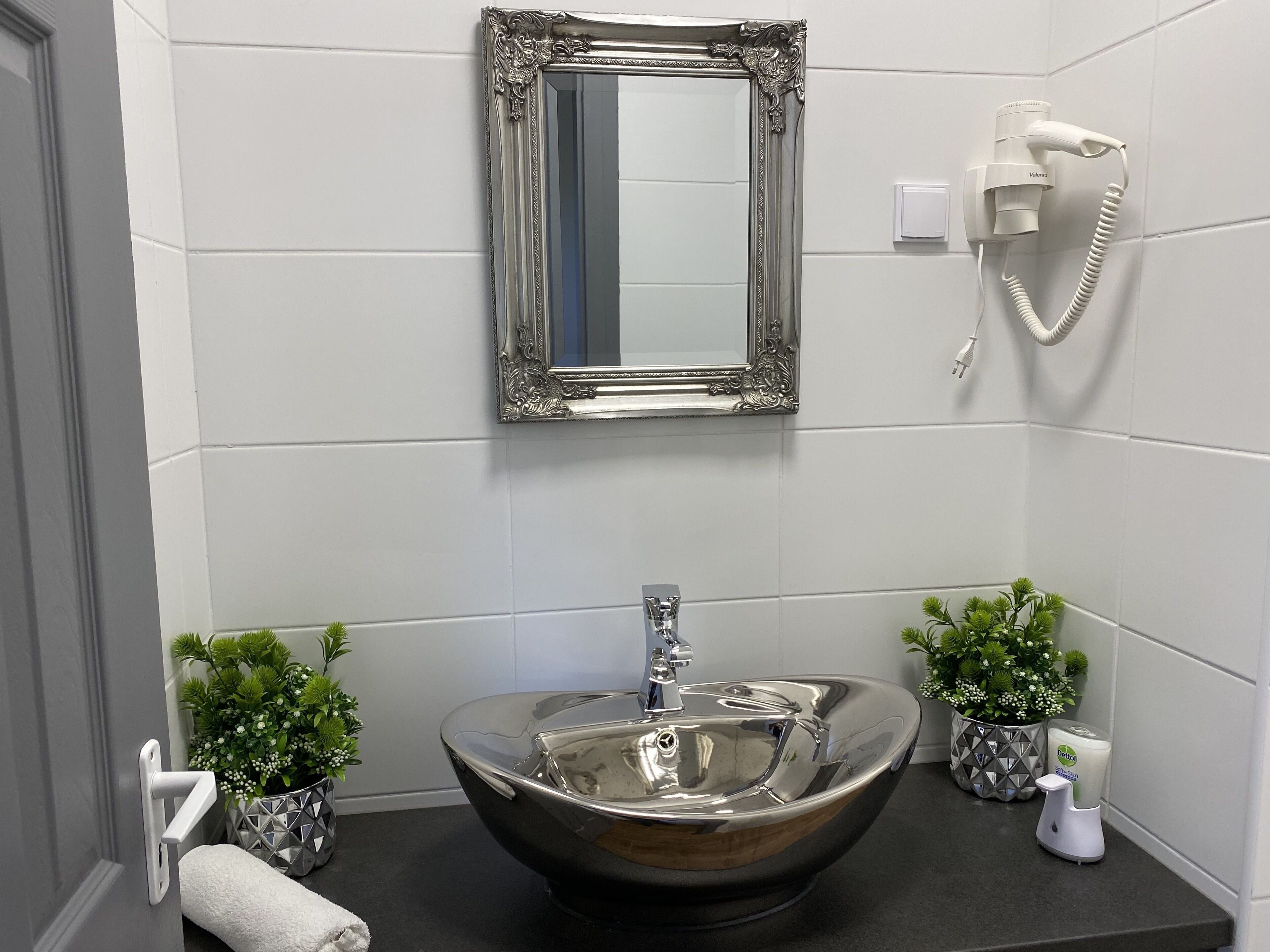 A bathroom with a large, ornate mirror, a modern sink, and a hairdryer mounted on the wall.