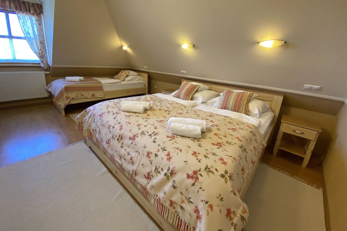 Un dormitorio con dos camas, ropa de cama floral, lámparas de noche y una ventana con cortinas.