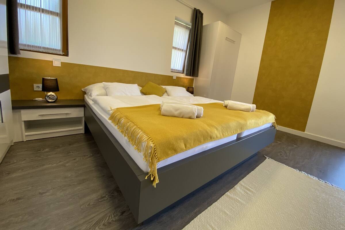 Un dormitorio moderno con una cama grande, mesitas de noche, una lámpara y vistas al exterior.