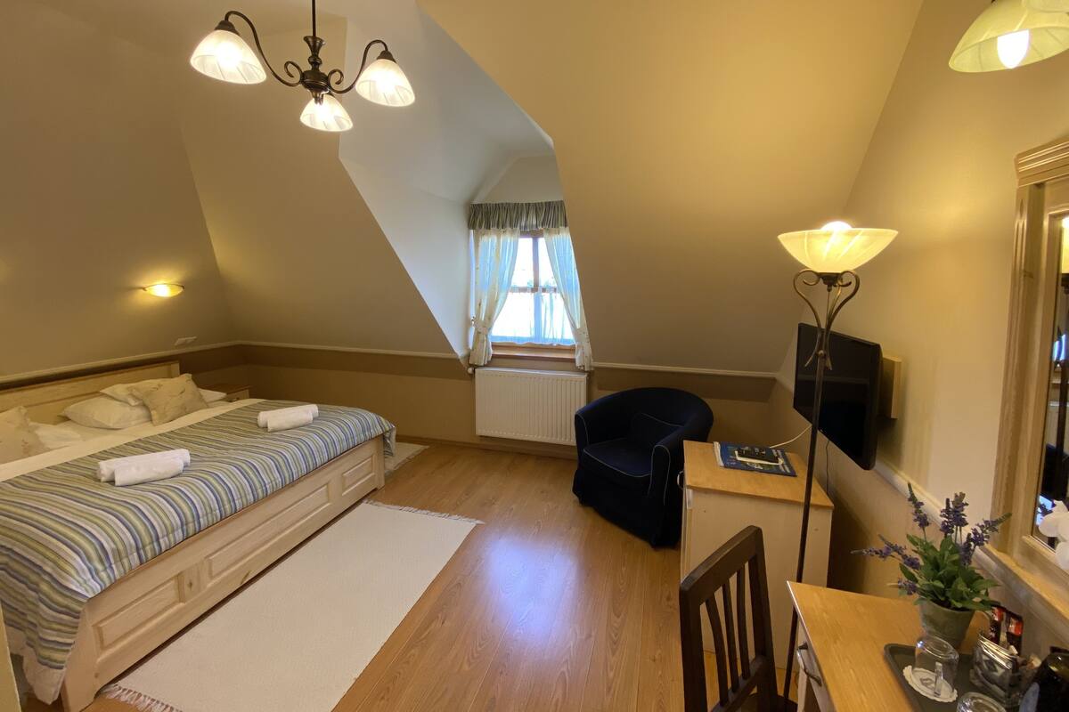 Un dormitorio con cama, escritorio, silla, lámpara y ventana con cortinas.