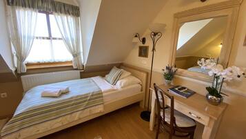 Ein Schlafzimmer mit Bett, Schreibtisch, Stuhl, Heizkörper, einem Fenster mit Vorhängen und einem Spiegel.