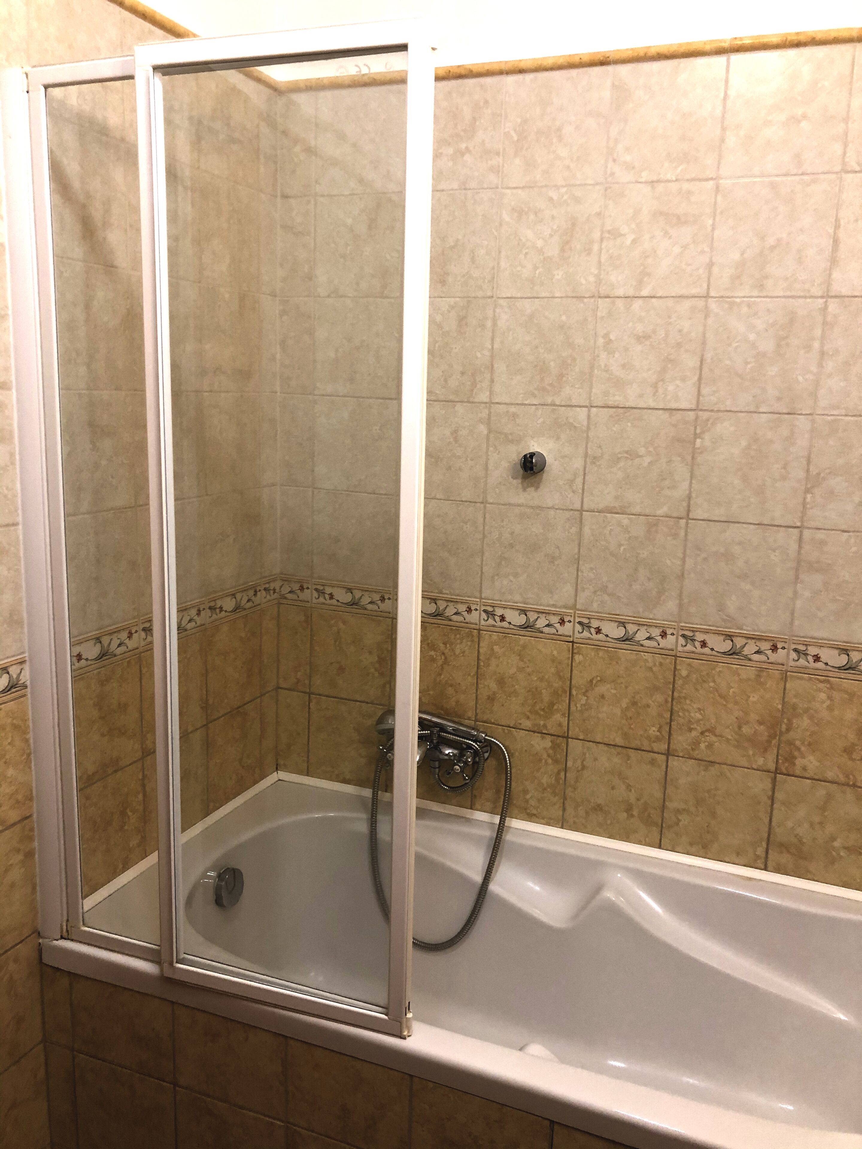 Un box de ducha con puerta de vidrio, un cabezal de ducha de mano y un grifo empotrado.