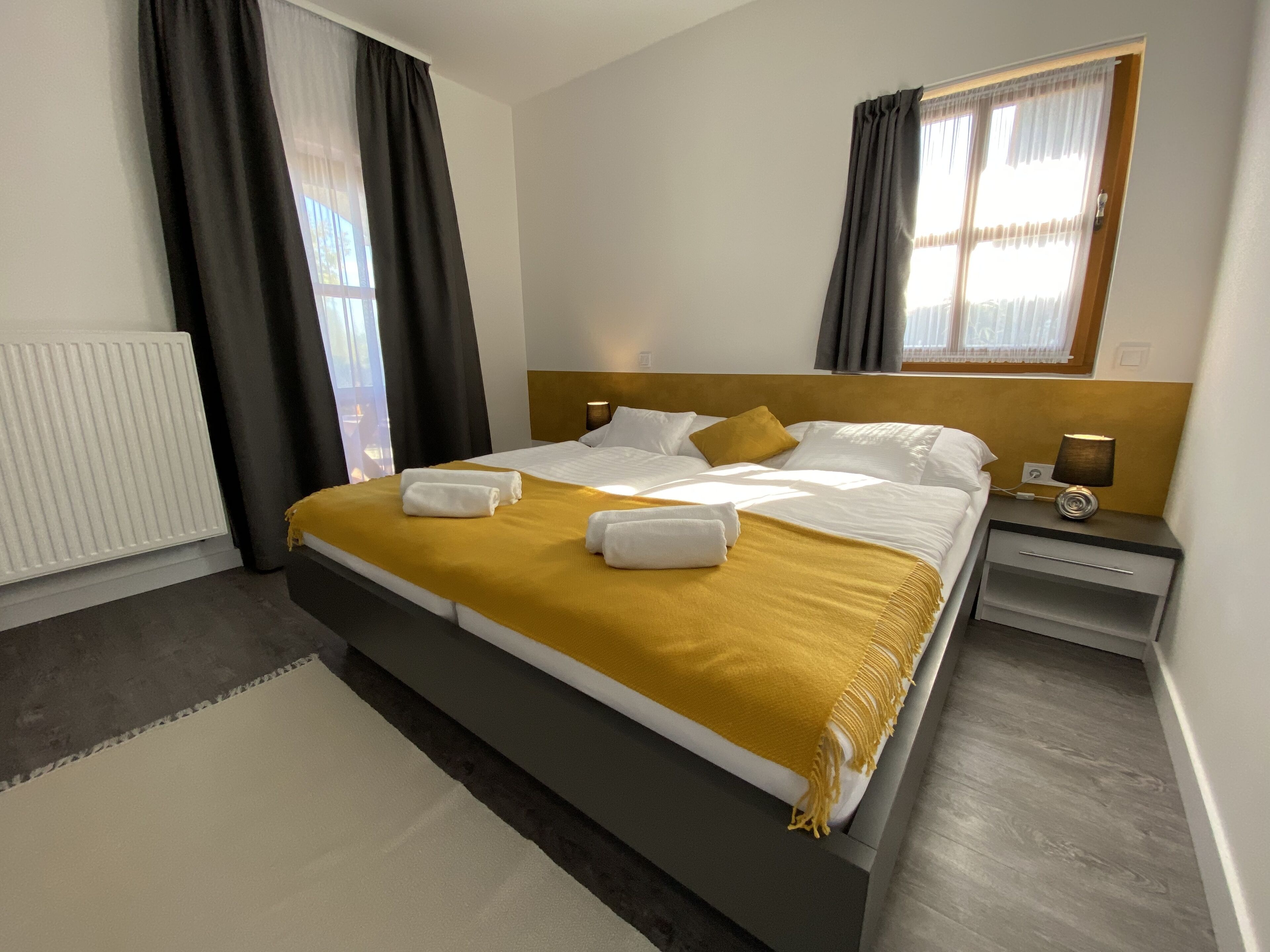 Habitación de hotel con una cama grande, una mesita de noche con lámpara y una ventana con cortinas.