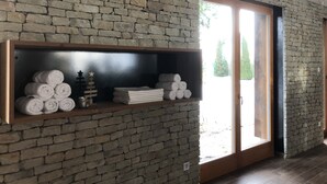 Una habitación con pared de piedra, estante de madera con toallas y puerta corredera de cristal que da al exterior.