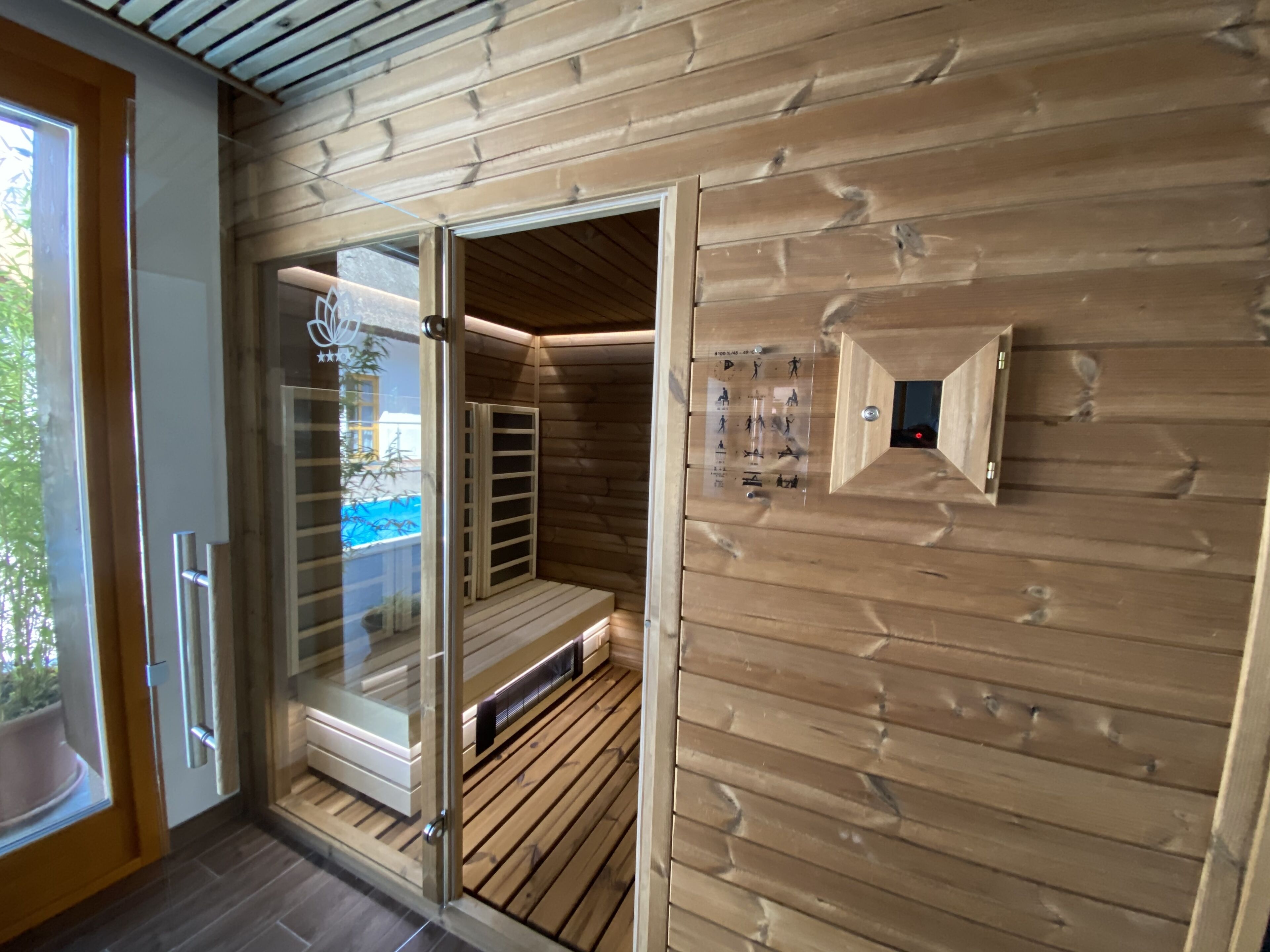 A sauna room with wooden walls, a glass door, and a control panel.