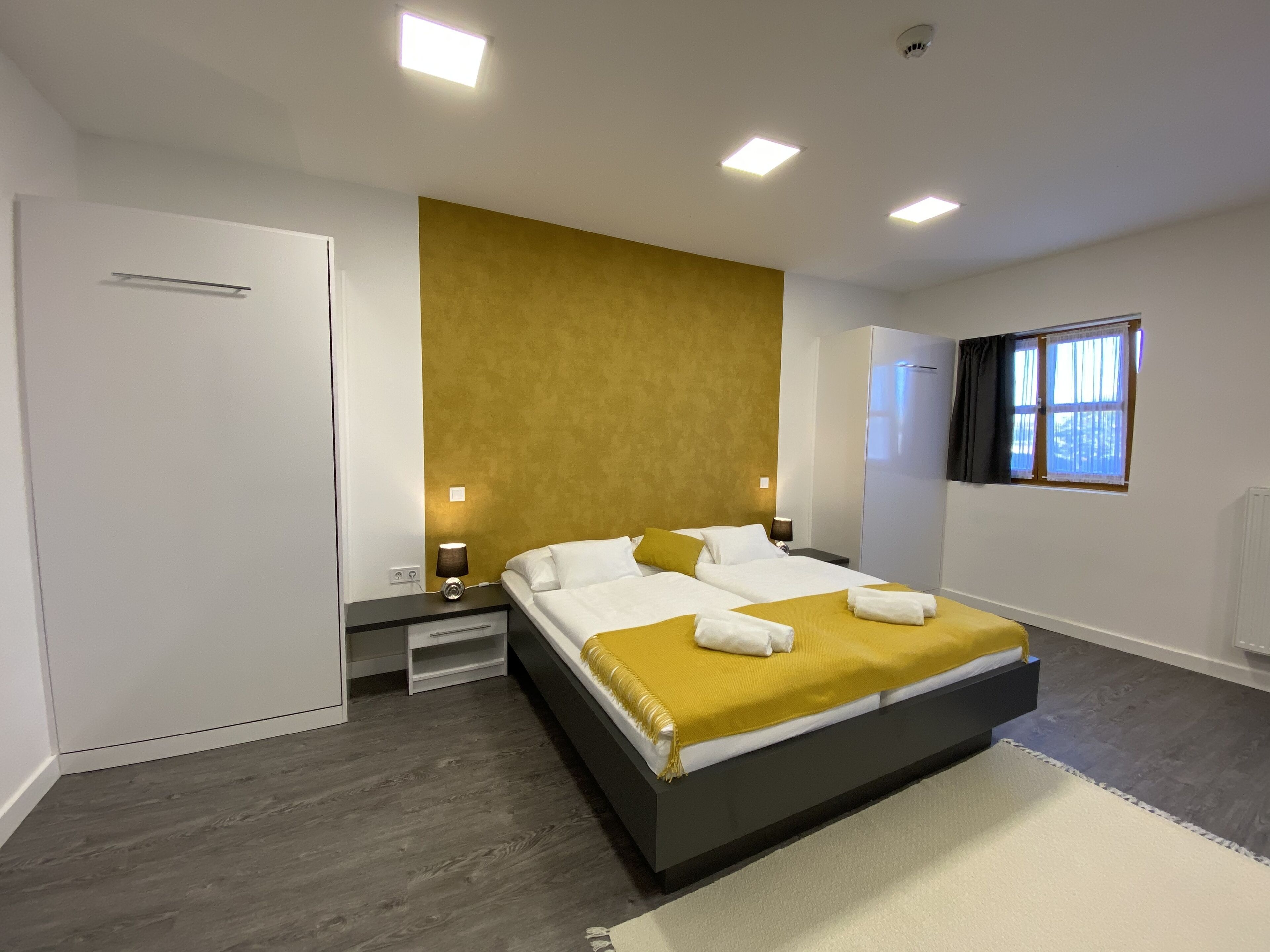 A modern bedroom with a large bed, bedside tables, a wardrobe, and a window with curtains.