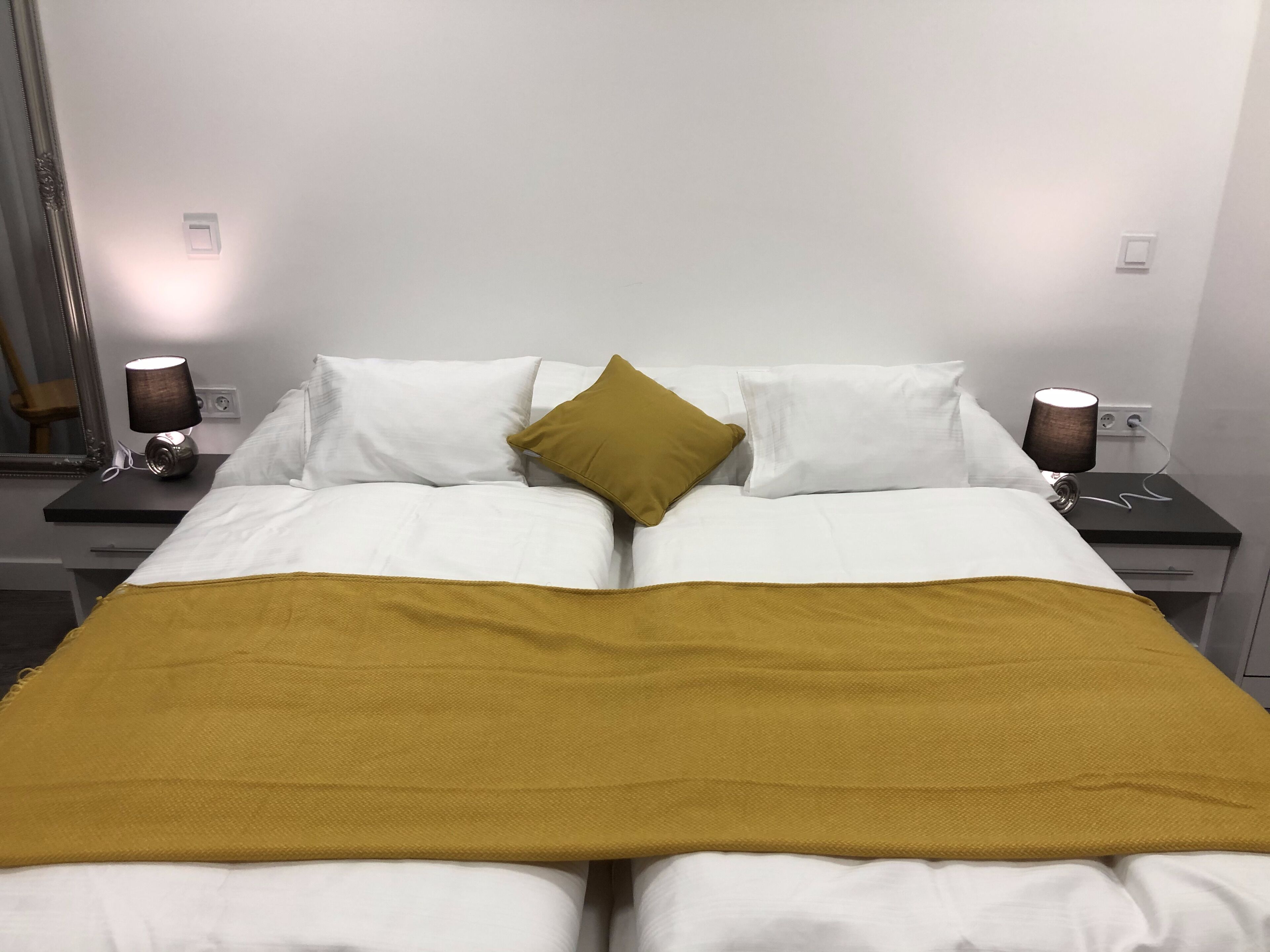 A double bed with white linens, a mustard-colored throw blanket, and two bedside lamps.