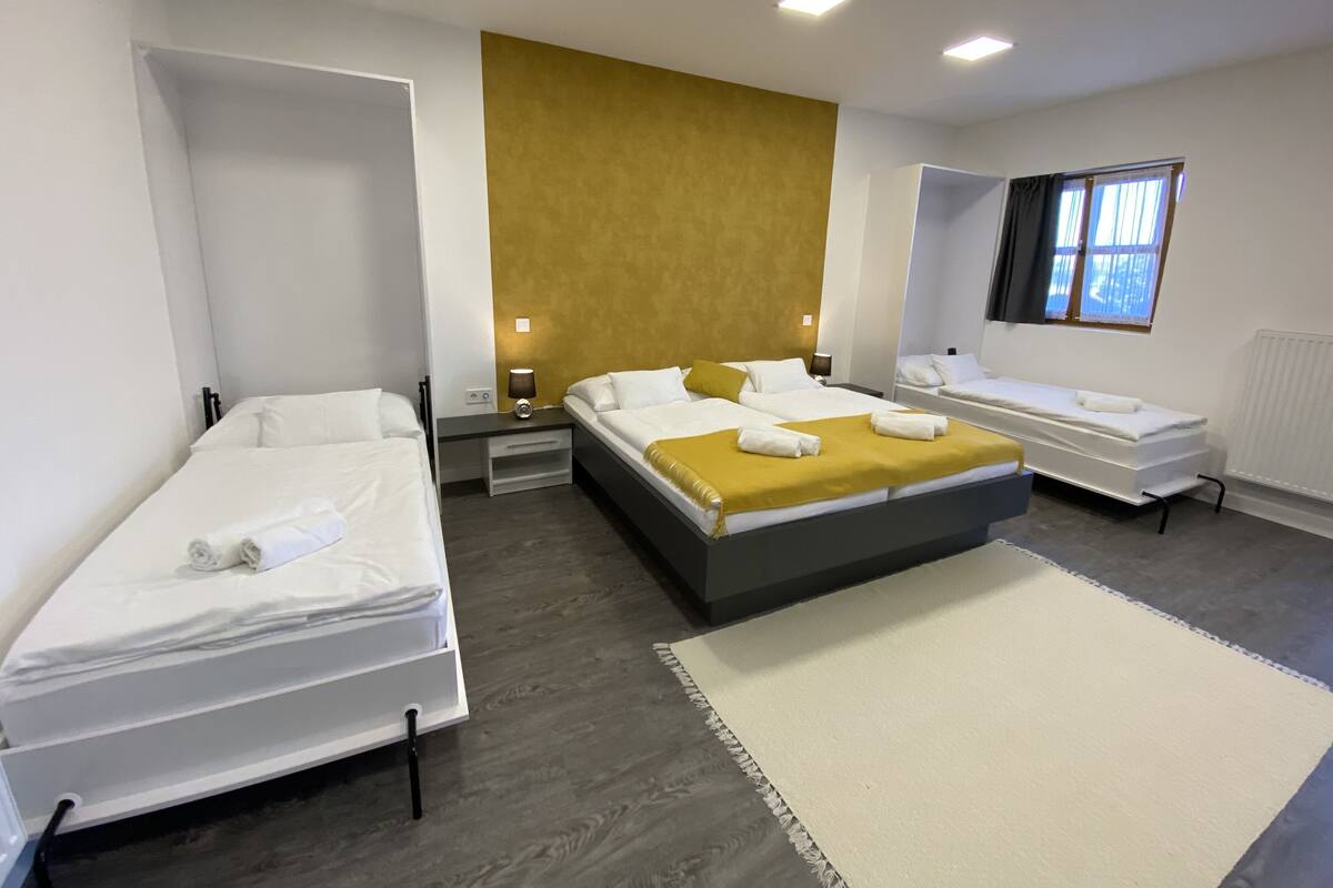 Habitación de hotel con tres camas, un ventanal grande y una alfombra blanca.
