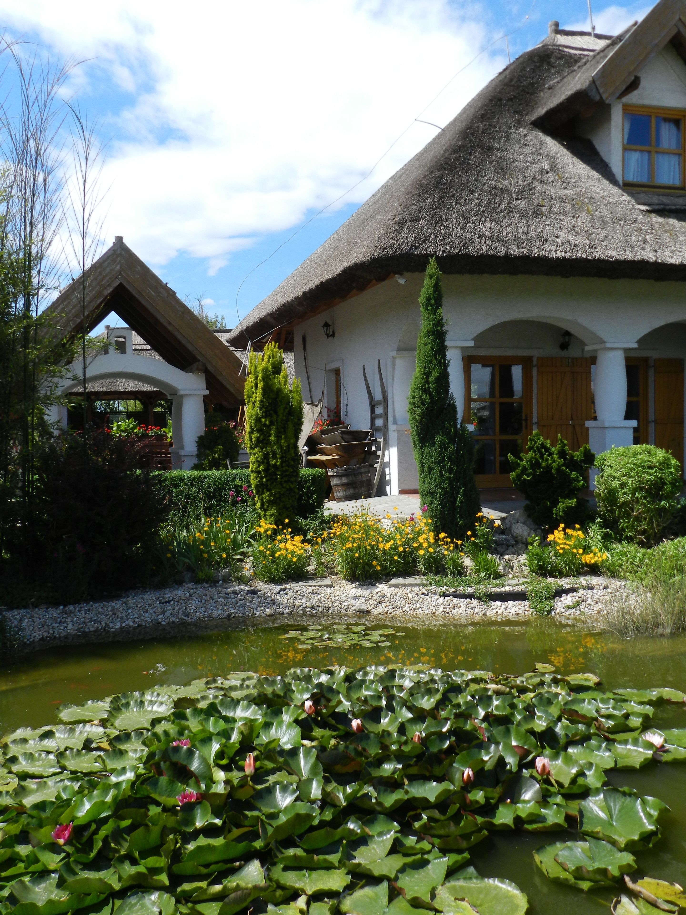 Una casa tradicional con techo de paja, un jardín con estanque y diversas flores.