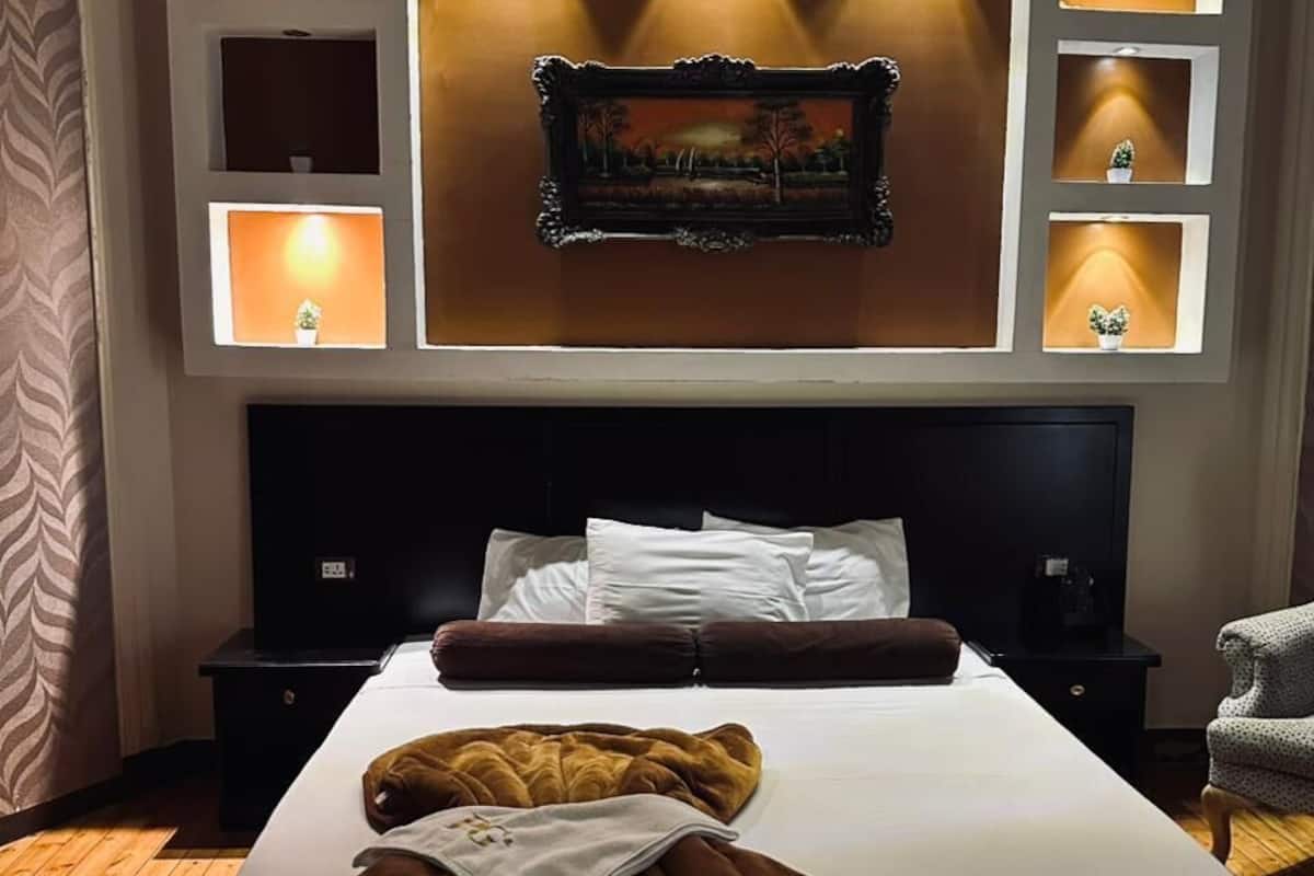 A hotel room with a large bed, a headboard with built-in lighting, a wall-mounted TV, and a bedside table with a lamp.