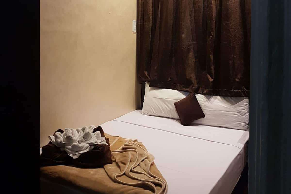 A single bed with white bedding, a brown blanket, and a decorative pillow. An air conditioning unit is mounted on the wall above the bed.