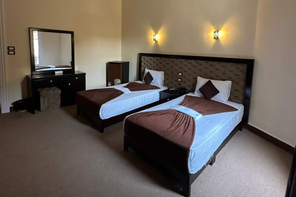 A hotel room with two beds, a dresser, a mirror, and wall sconces.