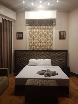 A hotel room with a large bed, a tufted headboard, a bench at the foot of the bed, a patterned curtain, and two bedside tables. - Paradise Boutique Hotel (Cairo)