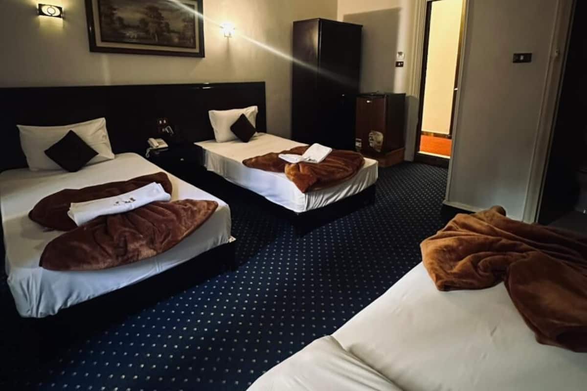 A hotel room with two beds, a dark carpet, a painting on the wall, and a door leading to another room.