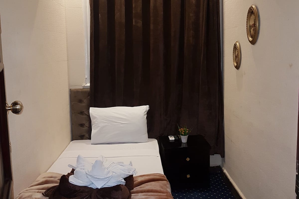 A hotel room with a bed, a nightstand, a wall clock, and a curtain.